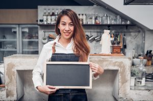 Asian female barista wear jean apron holding blank blackboard coffee menu